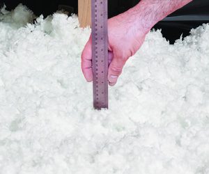 Closeup of hand using a ruler to measure the height of insulation in an attic floor.