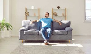 Man sitting in sun rays on the couch in the center of a minimalist living area.