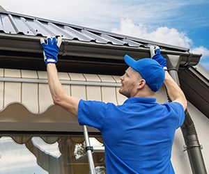 Man in a blue shirt installing gutters.