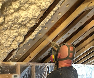 Man installing spray foam insulation in attic.