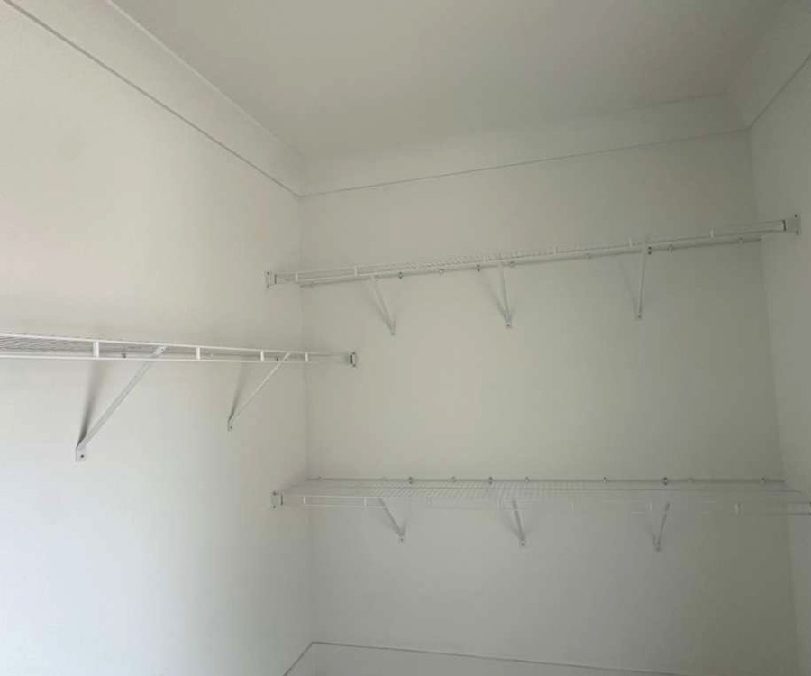 An empty walk-in closet featuring three levels of white wire shelving mounted on white walls.