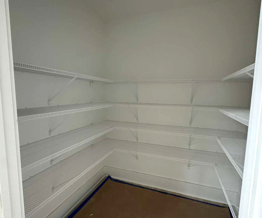 An empty walk-in closet or pantry featuring five tiers of white wire shelving wrap-around the white walls.